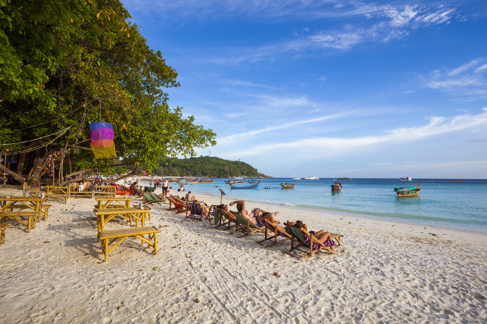 Satun, Thailand - March 12, 2011: People sunbathing in the shores of Koh Lipe beach in Satun, Thailand. Traditional longtail boats can be seen in the background.